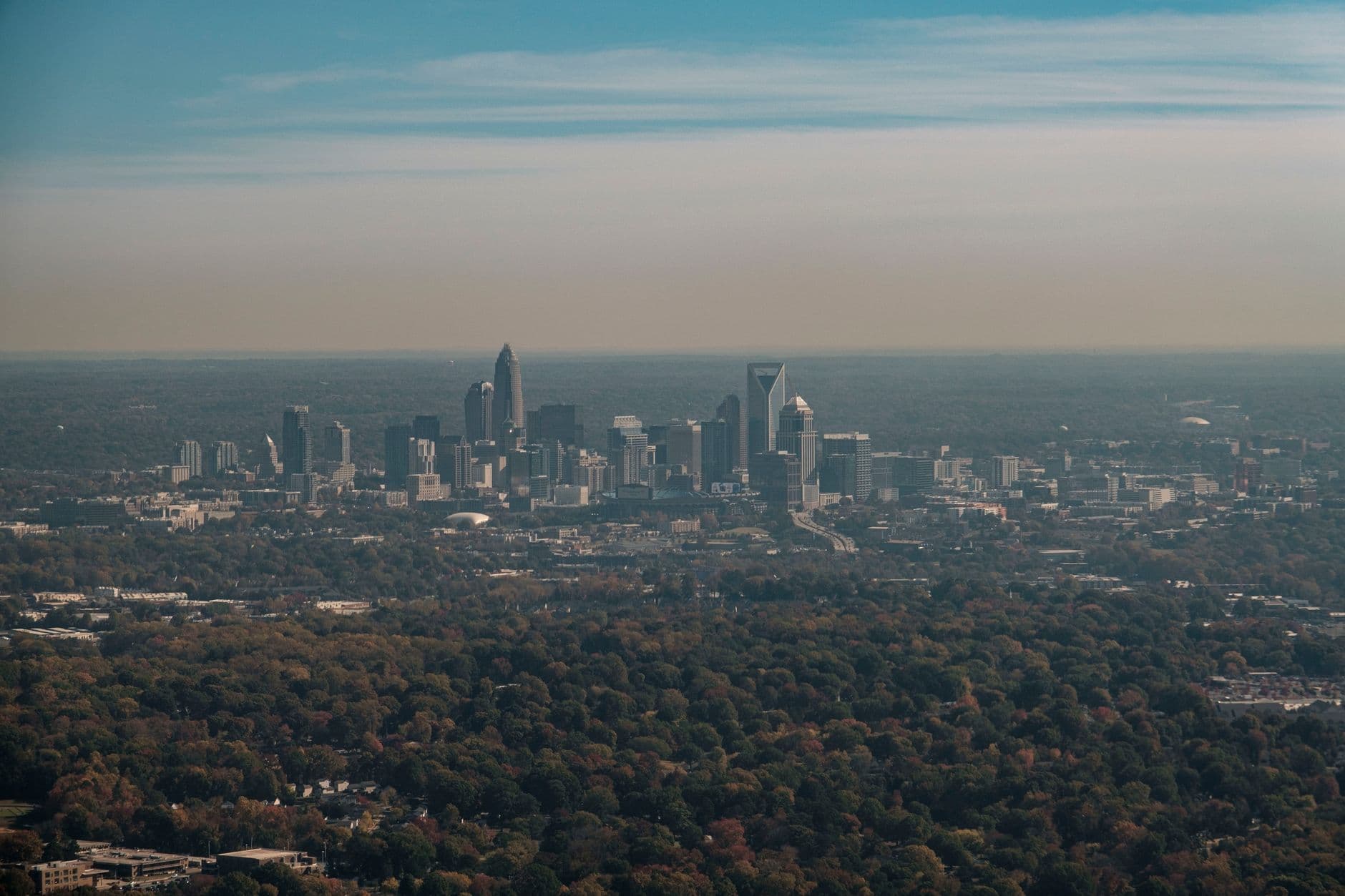 Stunning aerial shot of Charlotte skyline surrounded by fall foliage under a clear sky.