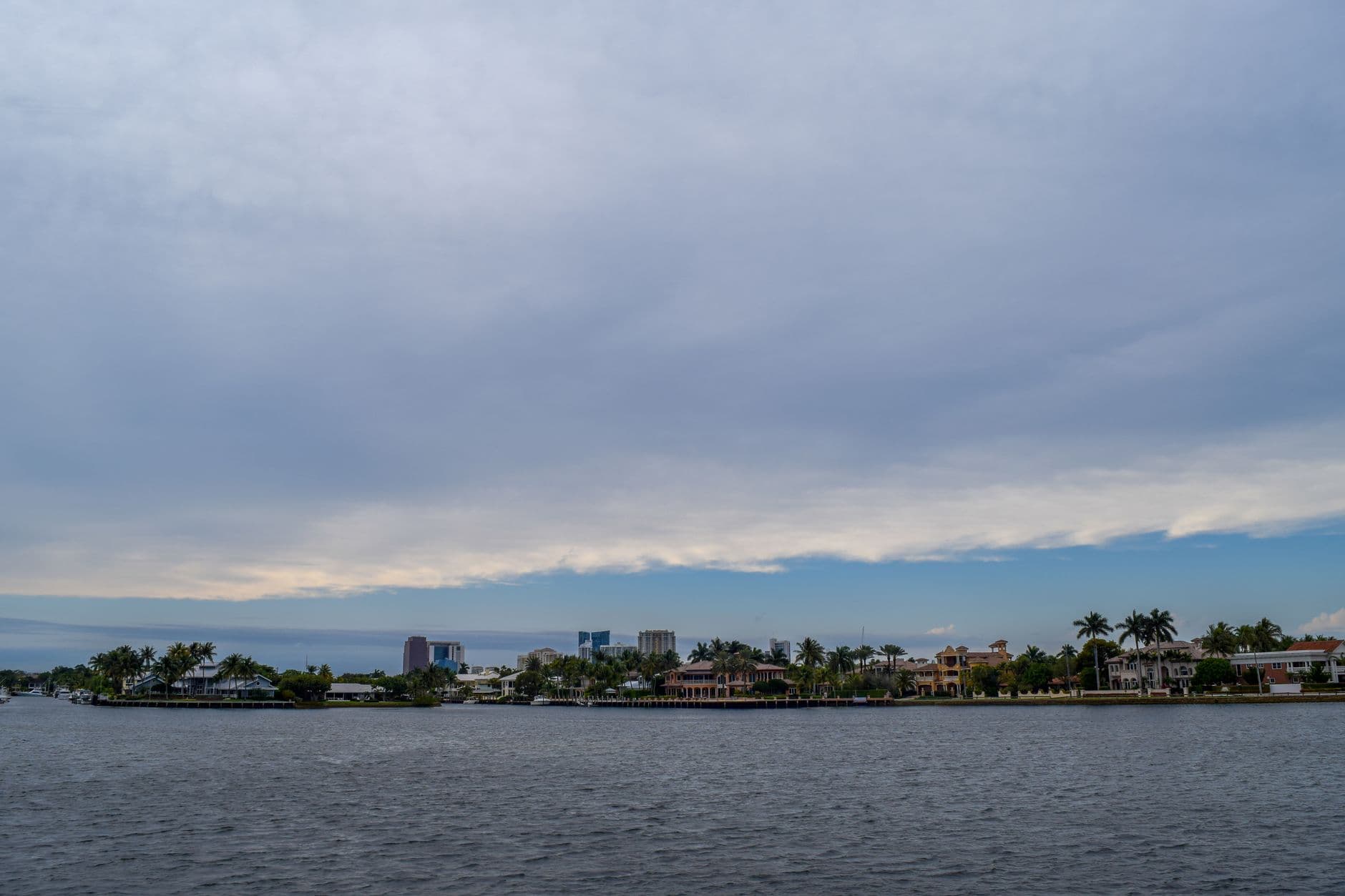 A tranquil coastal scene with tropical waterfront houses and palm trees under a cloudy sky.