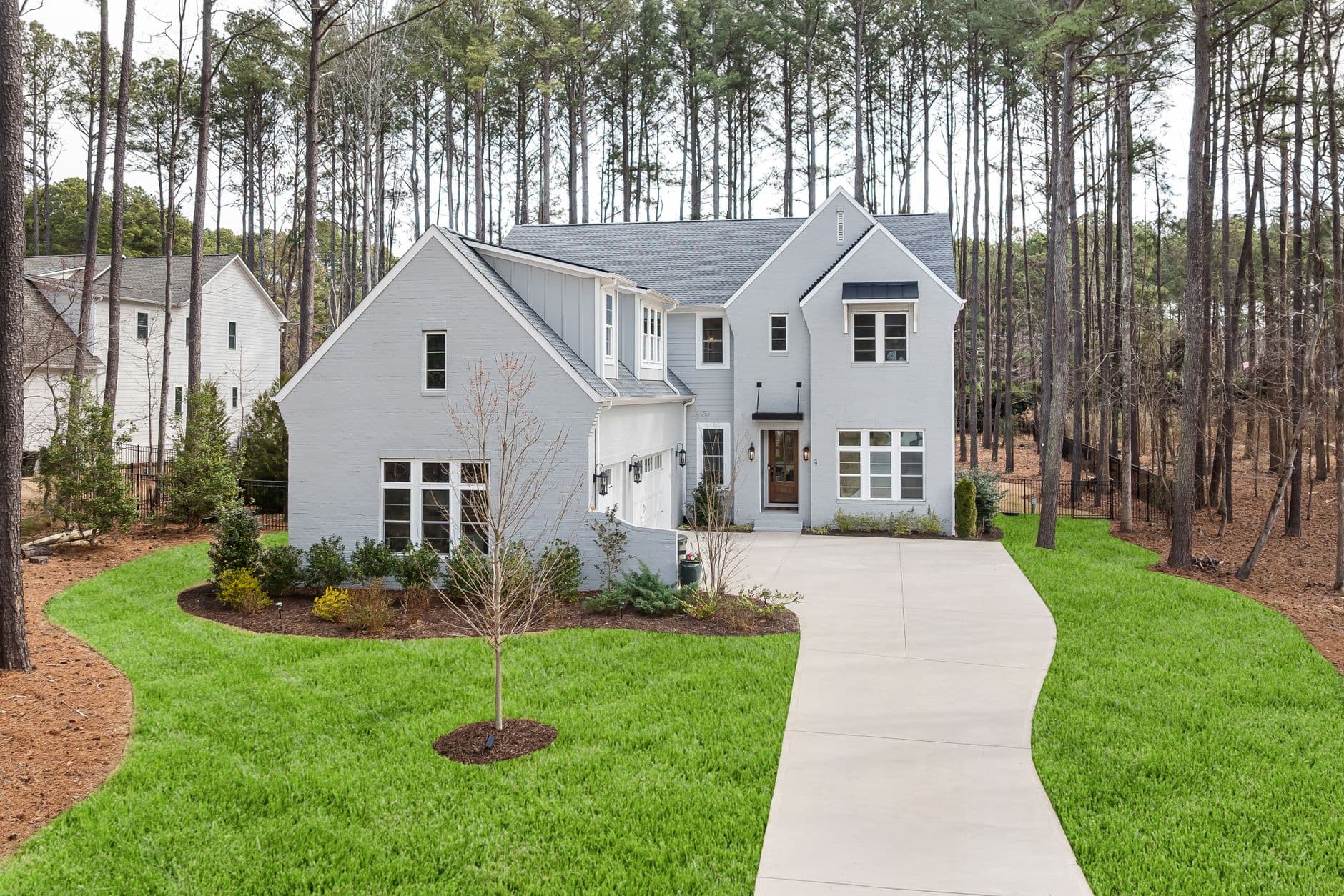 Elegant suburban home with gray siding and spacious driveway set amidst towering pine trees.