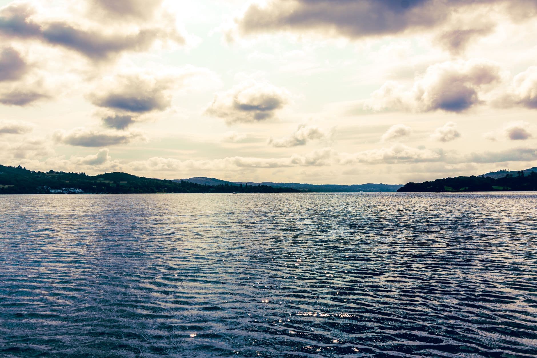 Peaceful Lake Windermere scene with calm waters and dramatic clouds in the scenic Lake District, England.